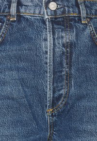 Blå denimjeans med knäppning, som har kontrasterande gula sömmar, framfickor och en strukturerad yta.