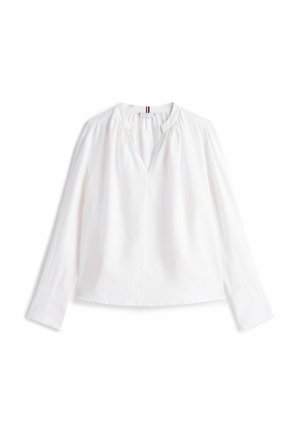 Blouse blanche à manches longues avec un col en V, détail froncé aux épaules et coupe décontractée ; tissu lisse avec une légère texture.