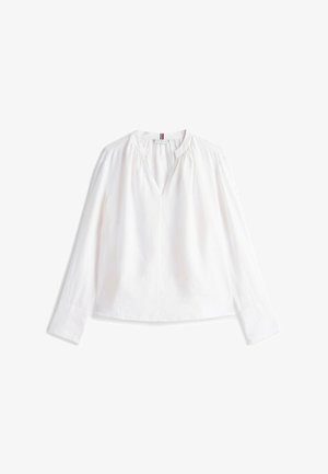 Blusa blanca de manga larga con escote en V, detalle fruncido en los hombros y corte holgado; tela suave con una ligera textura.