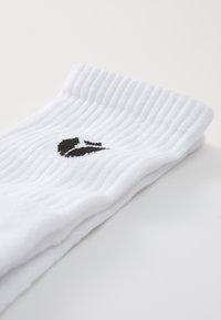 Calcetines blancos acanalados con un logo negro en el puño, hechos de una tela suave, con una apariencia texturizada y diseño doblado.