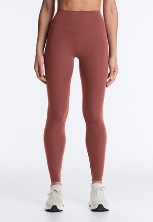 Slanktsiddende leggings i rustfarve med høj talje, båret med hvide ankelsokker og hvide snørestøvler på en person, der står.