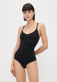 Μαύρη, εφαρμοστή ολόσωμη φόρμα με ρυθμιζόμενες τιράντες, στρογγυλή λαιμόκοψη και λείο υφή. Διαθέτει αδιάβροχο σχέδιο και μινιμαλιστικό στυλ.