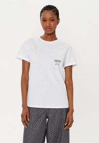 T-shirt bianca in cotone con maniche corte e scollatura rotonda. Presenta una tasca sul petto sinistro con il logo "LIU•JO" e il testo "EST. 1995".