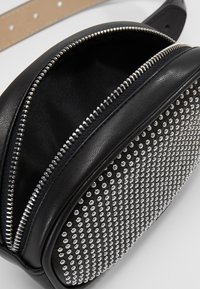 Schwarze Lederhandtasche mit einem mit Reißverschluss versehenen Fach, verziert mit silbernen Nieten auf der Vorderseite. Glatte Textur, runde Form, verstellbarer Schultergurt.