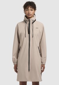 Giacca leggera beige con colletto alto, cordini regolabili, zipper frontale e due tasche laterali, con dettagli neri e branding.
