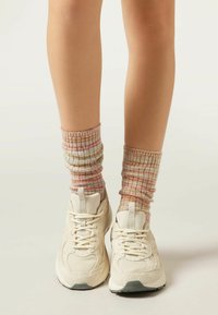 Beżowe sportowe sneakersy z teksturowanej siateczki i zamszowymi wstawkami, połączone z wielokolorowymi, prążkowanymi skarpetami z różowo-beżowym wzorem.