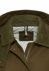 Olijfgroene jas met een corduroy kraag, ritssluiting aan de voorkant en gevoerde voering. Label binnenin geeft aan dat het van organisch materiaal is.
