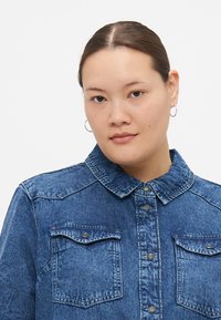 Donkerblauw denim overhemd met een klassieke kraag, knopen aan de voorkant en twee borstzakken met klep, van textuurstof.