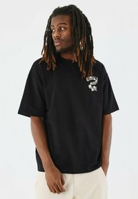 Zwarte oversized t-shirt van katoen, met korte mouwen en een grafische print op de borst. Soepele textuur, casual ontwerp.