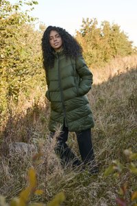 Geacă puffer verde măsliniu cu închidere prin fermoar, guler înalt și buzunare laterale, purtată peste pantaloni negri într-un cadru natural în aer liber.