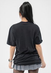 Black oversized t-shirt with short sleeves and a round neckline, paired with a pleated checkered skirt. Smooth texture and casual fit.