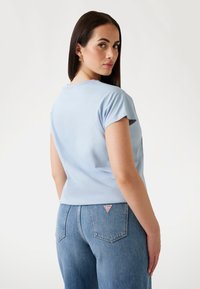 T-shirt kratkih rukava u nebeskoplavoj boji s okruglim izrezom, u kombinaciji s svijetloplavim trapericama koje imaju crvenu i bijelu oznaku na stražnjem džepu.