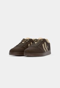 Sneakers in camoscio marrone con accenti beige, punta rotonda, design con lacci e suola in gomma testurizzata, caratterizzati da due strisce laterali.