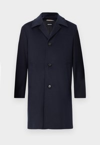 Cappotto di lana blu navy con silhouette dritta, ampi rever, chiusura con bottoni, tasche laterali e una texture liscia. Progettato per abbigliamento formale.