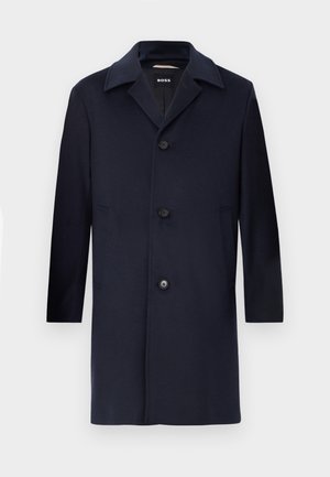 Manteau en laine marine avec une silhouette droite, grands revers, fermeture à boutons, poches latérales et une texture lisse. Conçu pour une tenue formelle.