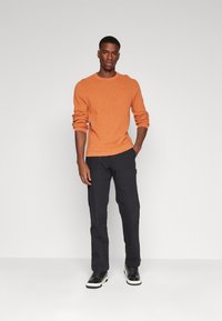 Oranžový pletený sveter s okrúhlym výstrihom, skombinovaný s čiernymi slim-fit nohavicami a čiernymi teniskami. Hladká textúra, priliehavý strih.