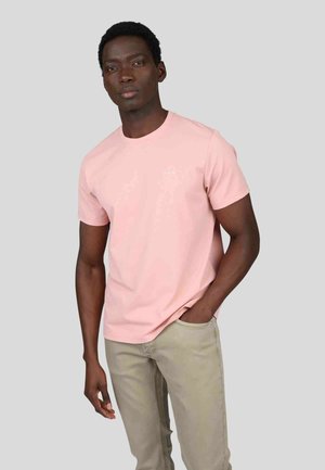 T-shirt rose pâle à manches courtes avec un col rond, fabriqué en tissu doux, doté d'un petit logo sur la poitrine. Porte avec un pantalon kaki clair.