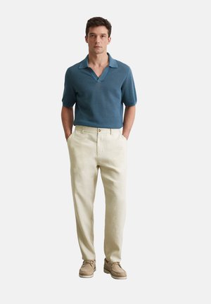 Korte mouwen, gebreide marineblauwe poloshirt met een brede kraag, gecombineerd met lichte beige linnen broeken en casual beige schoenen.