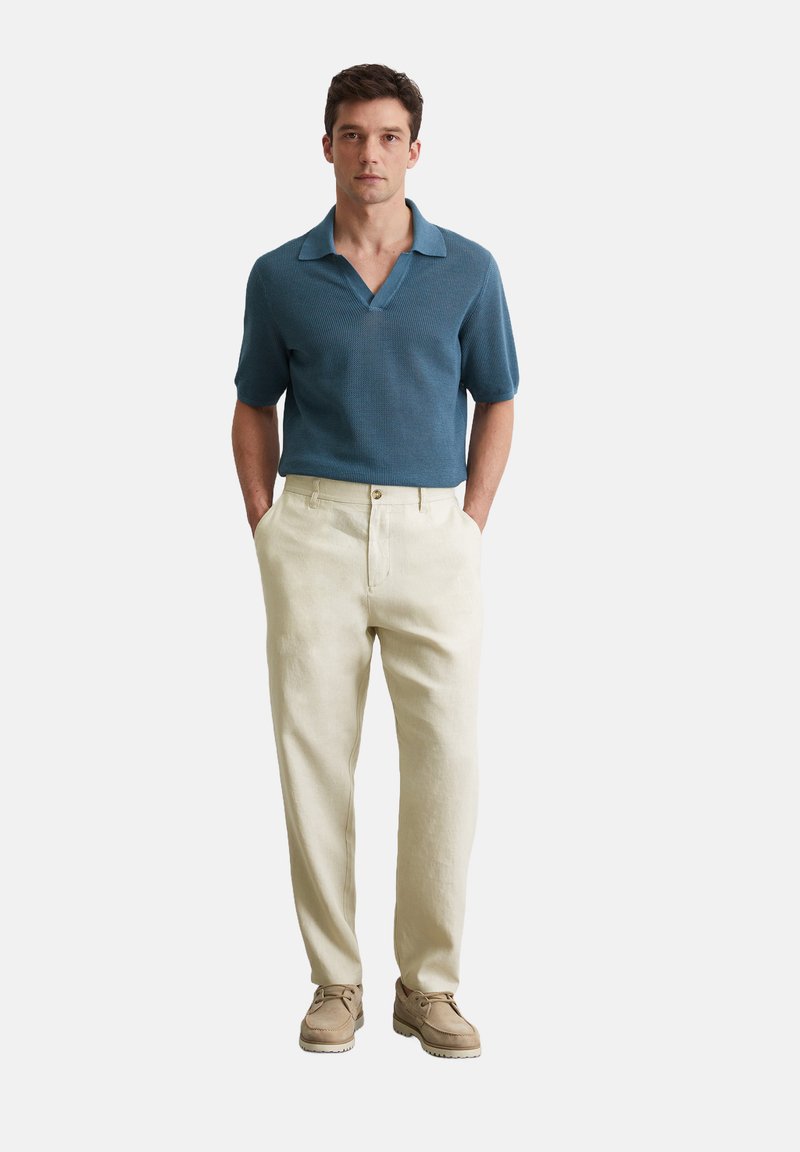 Polo shirt bleu marine à manches courtes et texturé avec un large col, associé à un pantalon en lin beige clair et des chaussures décontractées beiges.