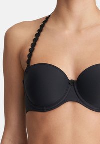 Black underwire bra with smooth fabric, molded cups, and scalloped strap detail. Center front features a round black accent button.