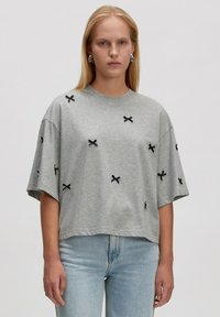 Graues, oversize T-Shirt aus Baumwolle mit schwarzer Kreuzstickerei. Kurze Ärmel im entspannten Schnitt und runder Ausschnitt.