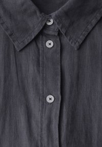 Szara lniana koszula z wysmukłym kołnierzykiem i trzema guzikami na listwie. Tekstura jest lekko pomarszczona i przewiewna.