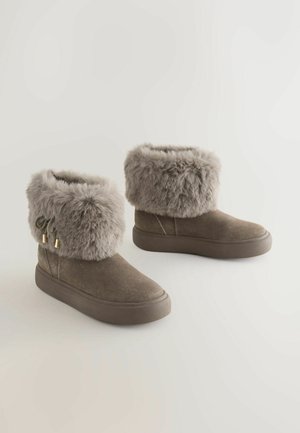 Rjave semishkane škornje z mehkimi, sivimi umetnimi krznom na robu, opremljene z zlatimi dodatki in ravnim gumijastim podplatom za stabilnost.