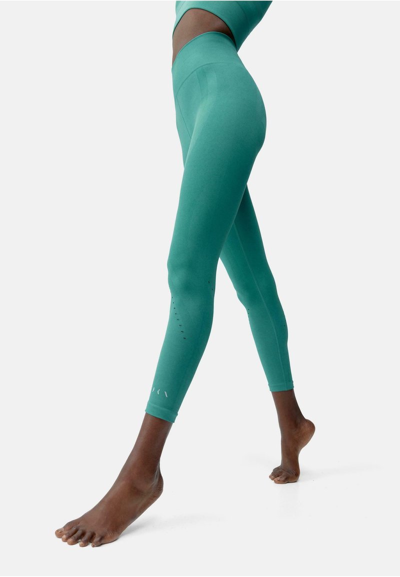 Teal värvi legginsid, mis on valmistatud venivast kangast, kõrge vöökoha, sileda pinna ja dekoratiivsete väikeste lõigetega sääreosas.
