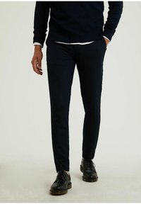 Navyblauwe slim-fit broek van zachte stof, met een gladde textuur en subtiele stiksels. Gedragen met zwarte veterschoenen.