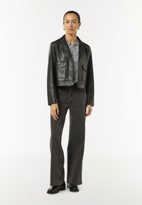 Schwarze Leder-Cropped-Jacke mit zwei vorderen Taschen, kombiniert mit einem schwarz-weißen gemusterten Oberteil. Getragen mit dunklen weiten Jeans und schwarzen Stiefeln.