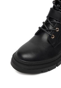 Melnas ādas potītes zābaki ar noapaļotu purngali, plakanu gumijas zoli un metāla aciņām šķiedru saitēm, ar gludu tekstūru un minimālu dizainu.