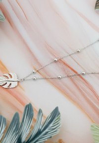 Söljd halsband med ett bladpendant på en fin kedja med runda pärlor, mot en mjukt färgad, marmorering bakgrund.