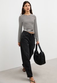 Randig långärmad topp i svart och vitt, kombinerad med högmidjade svarta jeans. En vävd svart handväska kompletterar looken tillsammans med flip-flops.