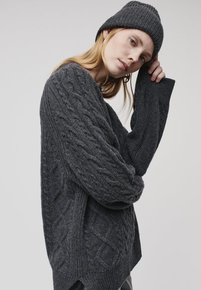 Maglione grigio scuro a coste con una vestibilità ampia e maniche inserite, abbinato a un berretto a coste coordinato, su uno sfondo neutro.