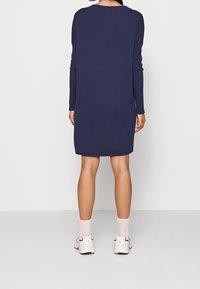 Robe tricotée marine à manches longues, coupe décontractée, encolure arrondie et ourlet légèrement effilé, assortie à des baskets blanches et bordeaux et des chaussettes.