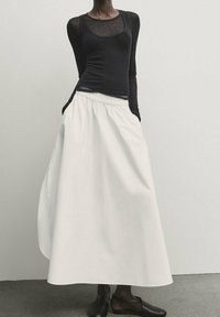 Top aderente nero a maniche lunghe abbinato a una gonna maxi bianca fluida, con vita elastica e design minimale, completato da scarpe nere.