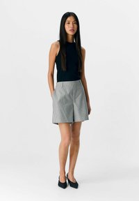 Sort ribbet top uden ærmer parret med gråstribede shorts med sidelommer, afsluttet med sorte spidse hæle. Enkel og moderne design.
