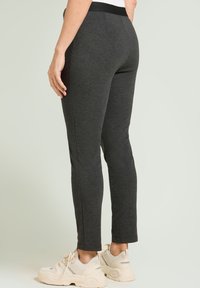 Leggings deportivos grises con un diseño ajustado, tobillos estrechos y una cinturilla elástica ancha, combinados con zapatillas de color claro.