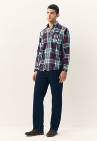 Chemise à carreaux rouge, verte et bleue, à boutons, avec col, poche et manches longues, associée à un jean bleu foncé et des bottes marron.