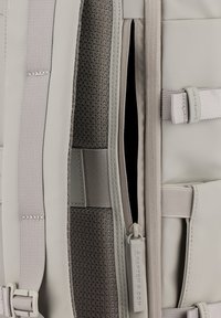 Zaino grigio con esterno liscio e morbido, dotato di zip, spallacci regolabili e interno in tessuto a fantasia. Accenti argentati visibili.
