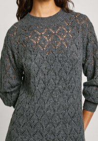 Pull en tricot gris avec un design ajouré à motifs en losange, col rond côtelé, et longues manches avec poignets roulés.