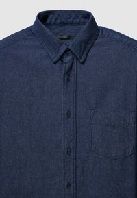 Camicia di jeans di colore blu scuro con chiusura a bottoni, colletto e taschino singolo sul petto. Presenta un tessuto testurizzato e un design a vestibilità standard.
