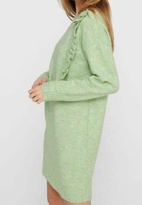Jasnozielona sukienka sweterkowa z prążkowanym dołem i falbanką po jednej stronie. Miękka w dotyku o nieco luźniejszym kroju.