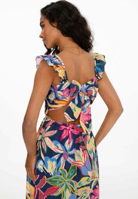 Šaty s květinovým potiskem, ruffled ramínky, mašlí na zadní části a otevřeným zadním designem. Barvy zahrnují modrou, růžovou, zelenou a žlutou.