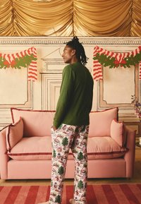 Grön långärmad tröja i kombination med mönstrade rosa pyjamasbyxor med julmotiv. En rosa soffa med röd kant syns i bakgrunden.