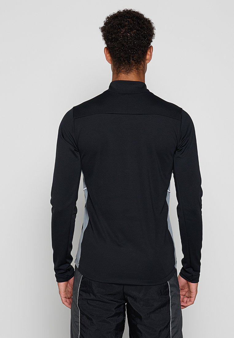 Camisa deportiva negra de manga larga con cuello alto y paneles laterales grises en contraste. Tejido suave con un diseño de corte ajustado.