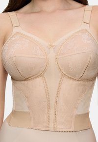 Bustier in pizzo beige con spalline regolabili, motivi floreali e un piccolo fiocco al centro, indossato sulla parte superiore del torso su sfondo neutro.