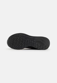Sole di una scarpa da ginnastica nera con motivi di battistrada geometrici triangolari e rettangolari su uno sfondo bianco.