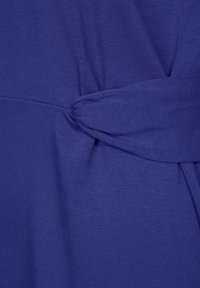 Haut violet en tissu doux, doté d'un accent noué sur le côté, avec une texture lisse et un design simple.