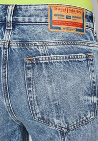 Blue denim jeans with a faded finish, visible stitching, and a rectangular brown label on the back, featuring brand and quality information.